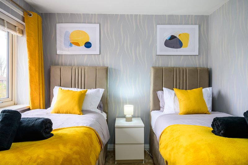 Twin bedroom with yellow bedding, beige headboards, abstract wall art, and black accent cushions