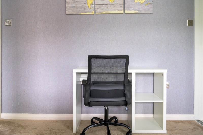 Minimalist home office with black mesh chair, white shelving unit and lavender walls