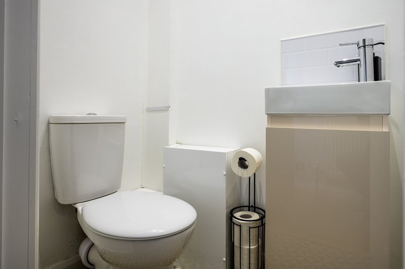 Modern bathroom with white toilet, wall-mounted sink, mirror and toilet paper holder