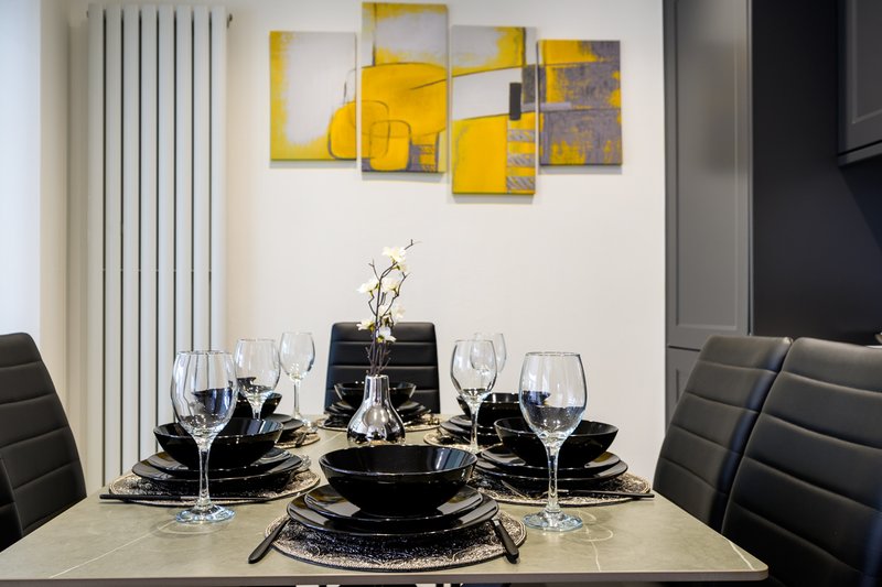 Modern dining room with set table, black place settings, wine glasses and yellow abstract wall art