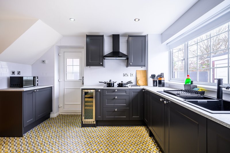 Modern kitchen with dark cabinetry, white countertops, island unit, and geometric floor tiles