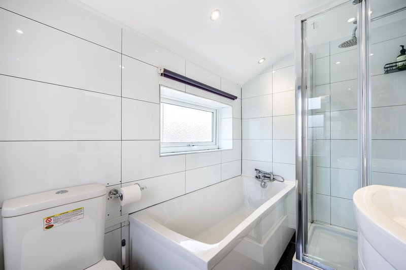 Modern bathroom with white tile walls, bathtub, shower enclosure and window