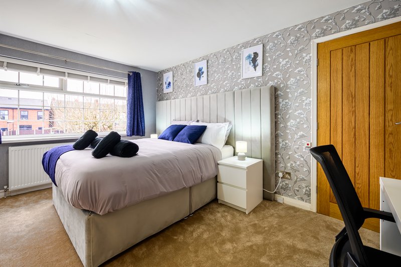 Bedroom with double bed, blue bedding, patterned wallpaper, wooden wardrobe and window view