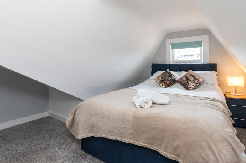 Attic bedroom with double bed, patterned cushions, rolled towels and bedside lamp