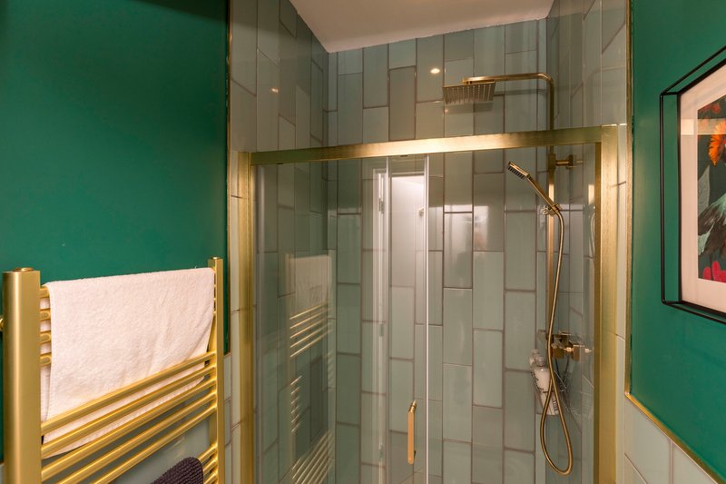 Modern bathroom with walk-in shower, green walls, gold fixtures and heated towel rail