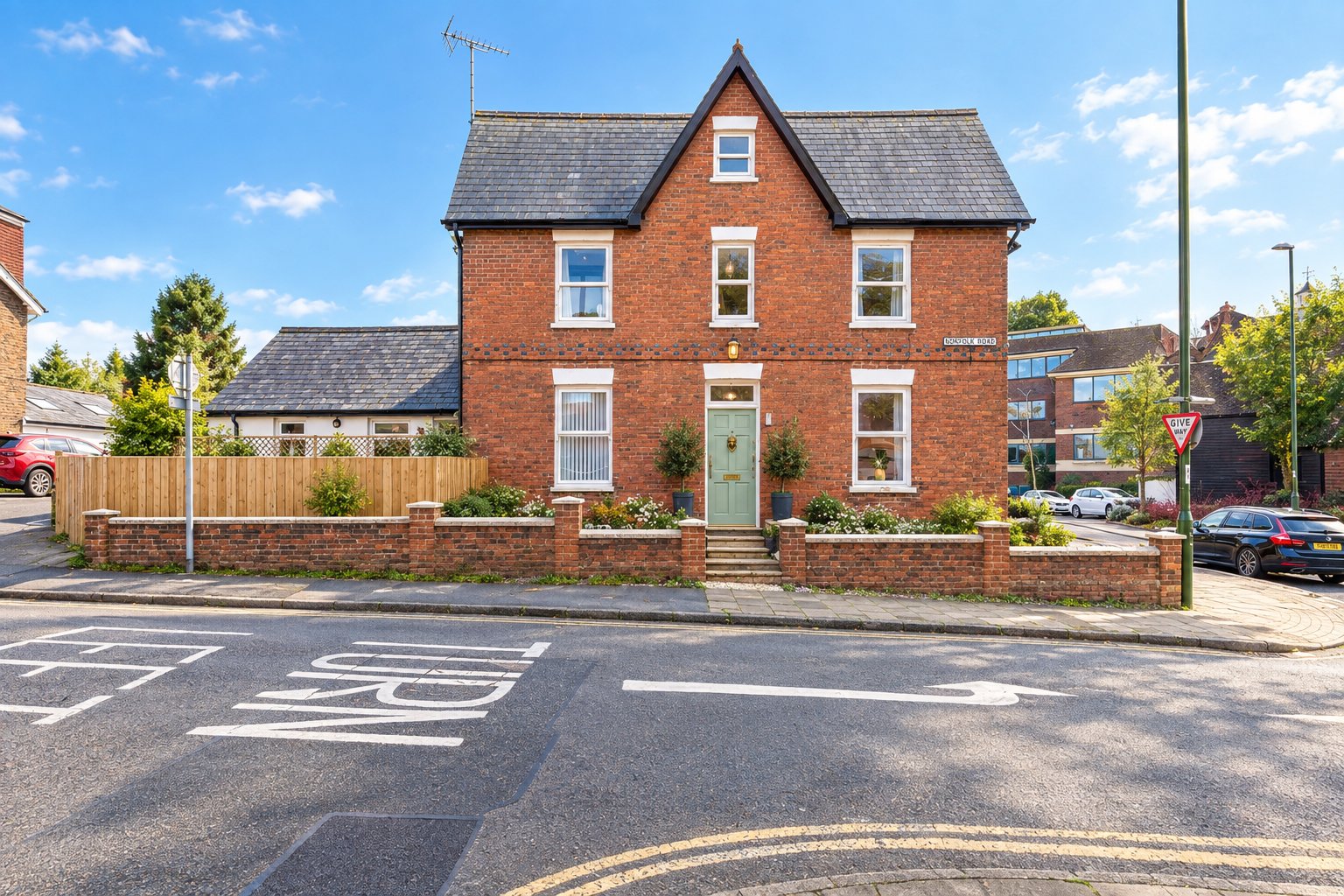 Red brick Victorian house with green door, multiple windows, front garden and driveway