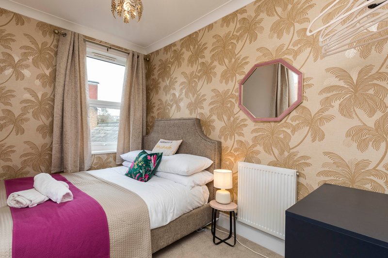 Bedroom with double bed, patterned wallpaper, pink circular mirror, and window with curtains