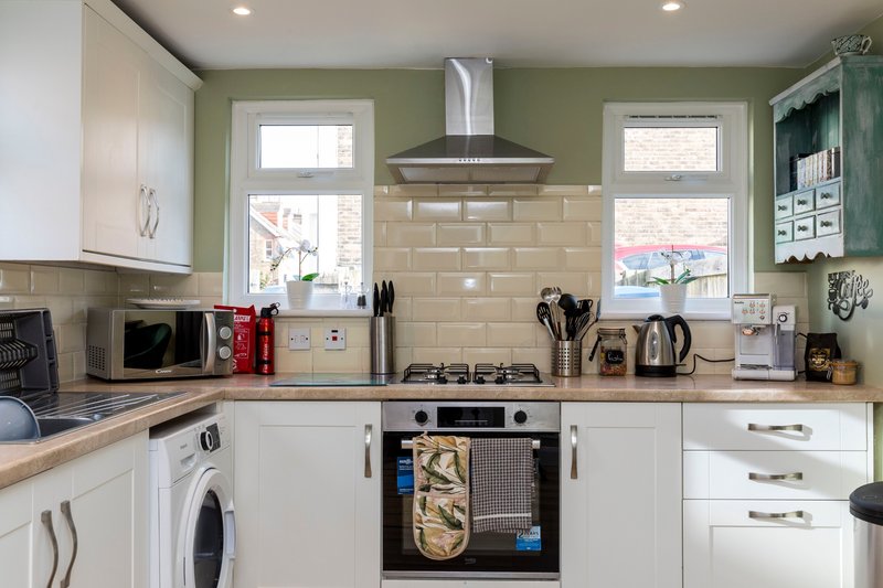 Modern kitchen with white cabinets, cream tile splashback, gas hob, and stainless steel extractor hood