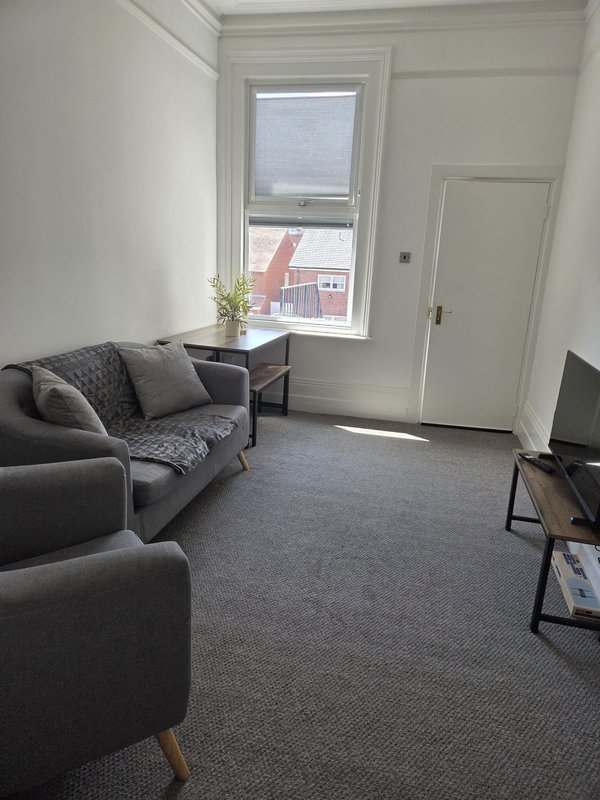 Modern lounge with dark grey sofas, small table, window overlooking street and brick building