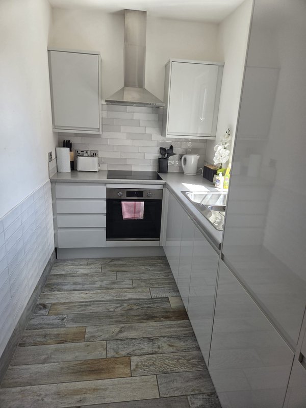 Modern galley kitchen with white cabinetry, stainless steel range hood, subway tile backsplash and wood-effect flooring