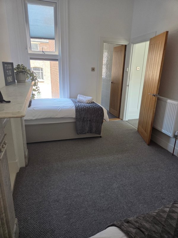 Bedroom with single bed, desk, wooden doors, and window overlooking street