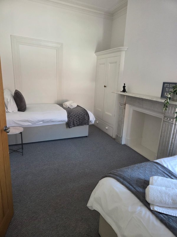 Bedroom with two single beds, white wardrobe, fireplace and dark grey carpet