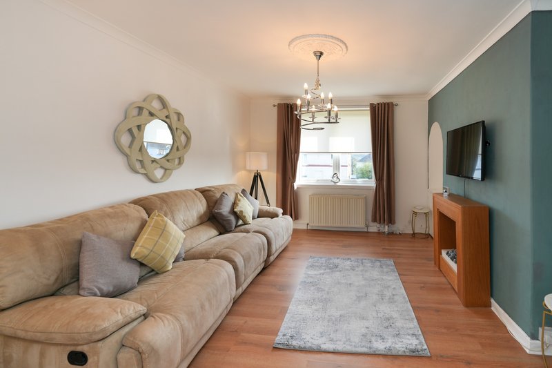 Spacious living room with beige sofa, wooden floor, wall-mounted TV, and teal accent wall