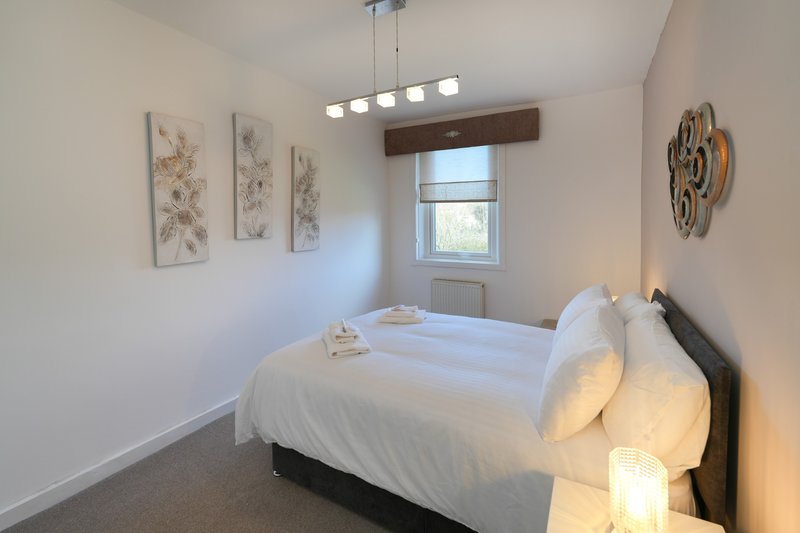 Bright modern bedroom with double bed, white bedding, pendant lighting and botanical wall art