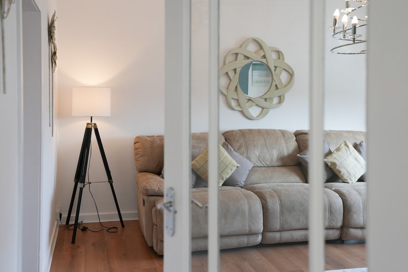 Modern living room with gray sofa, decorative mirror, tripod floor lamp and wooden flooring