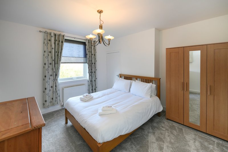 Bright bedroom with double bed, wooden furniture, wardrobe and window with patterned curtains