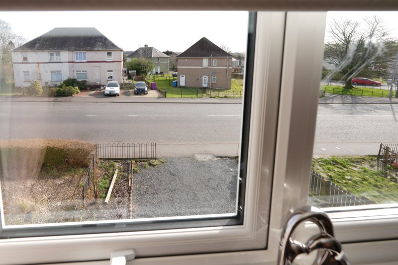 Street view through window showing residential buildings, driveway and garden fence