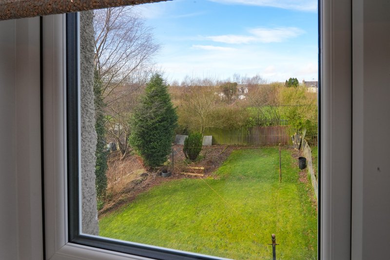 View through window of garden with lawn, trees, fence and countryside beyond