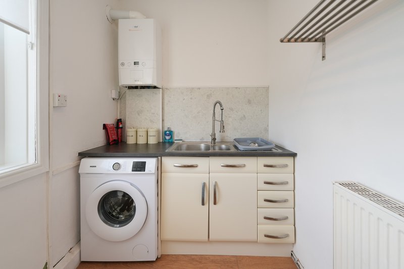 Compact utility room with washing machine, cream cabinetry, sink, and boiler