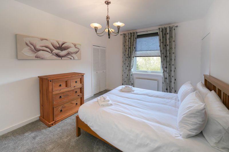 Bright bedroom with double bed, wooden furniture, window with patterned curtains and wall art