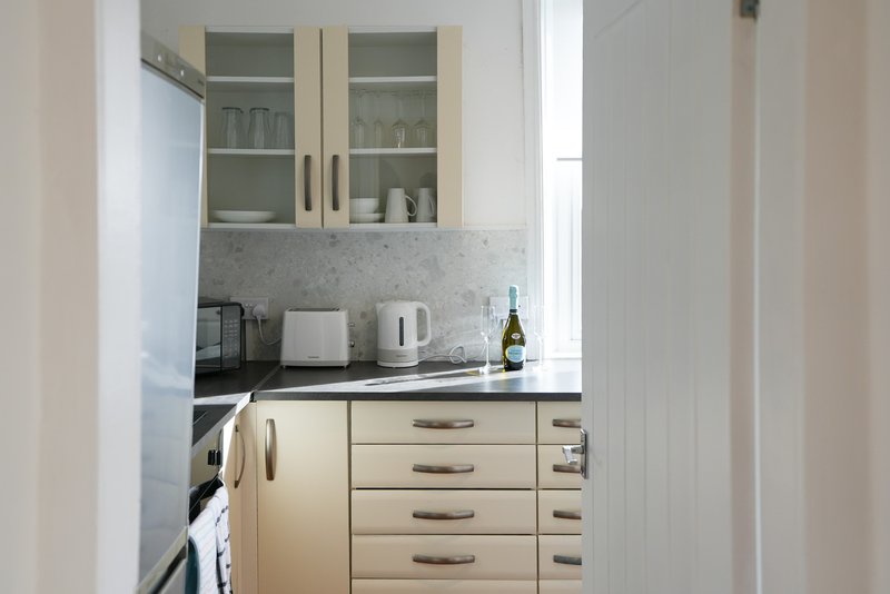 Compact modern kitchen with cream cabinets, grey countertop and white appliances