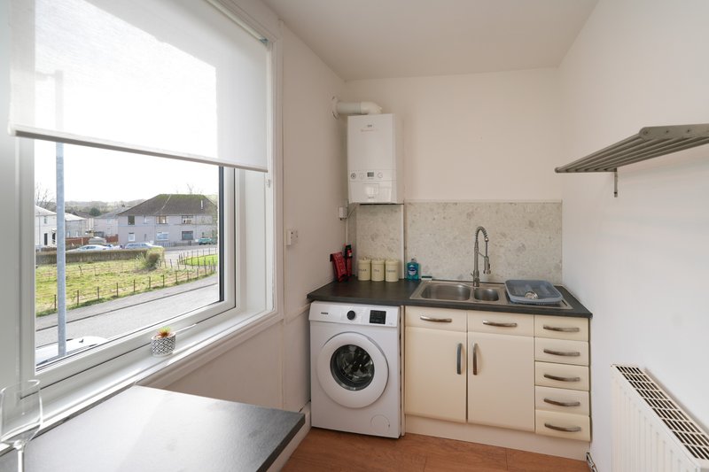 Kitchen with washing machine, sink, cabinets and large window overlooking garden