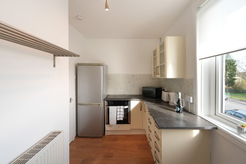 Modern kitchen with wooden flooring, stainless steel appliances, dark countertop and window view