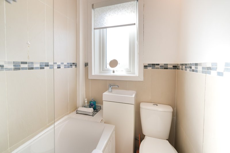 Bathroom with bathtub, toilet, sink, window and tiled walls
