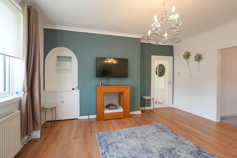 Modern living room with teal accent wall, wooden fireplace, wall-mounted TV and chandelier