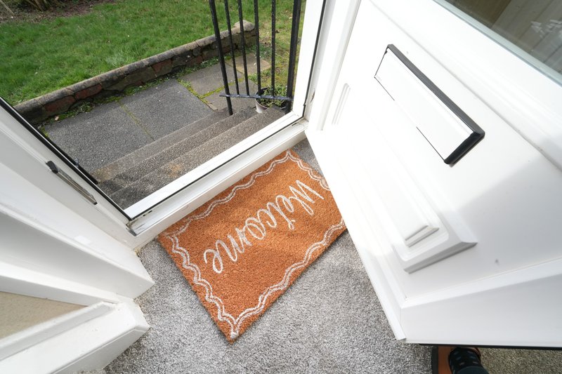 Entrance doorway with brown welcome mat, white door frame, and garden view