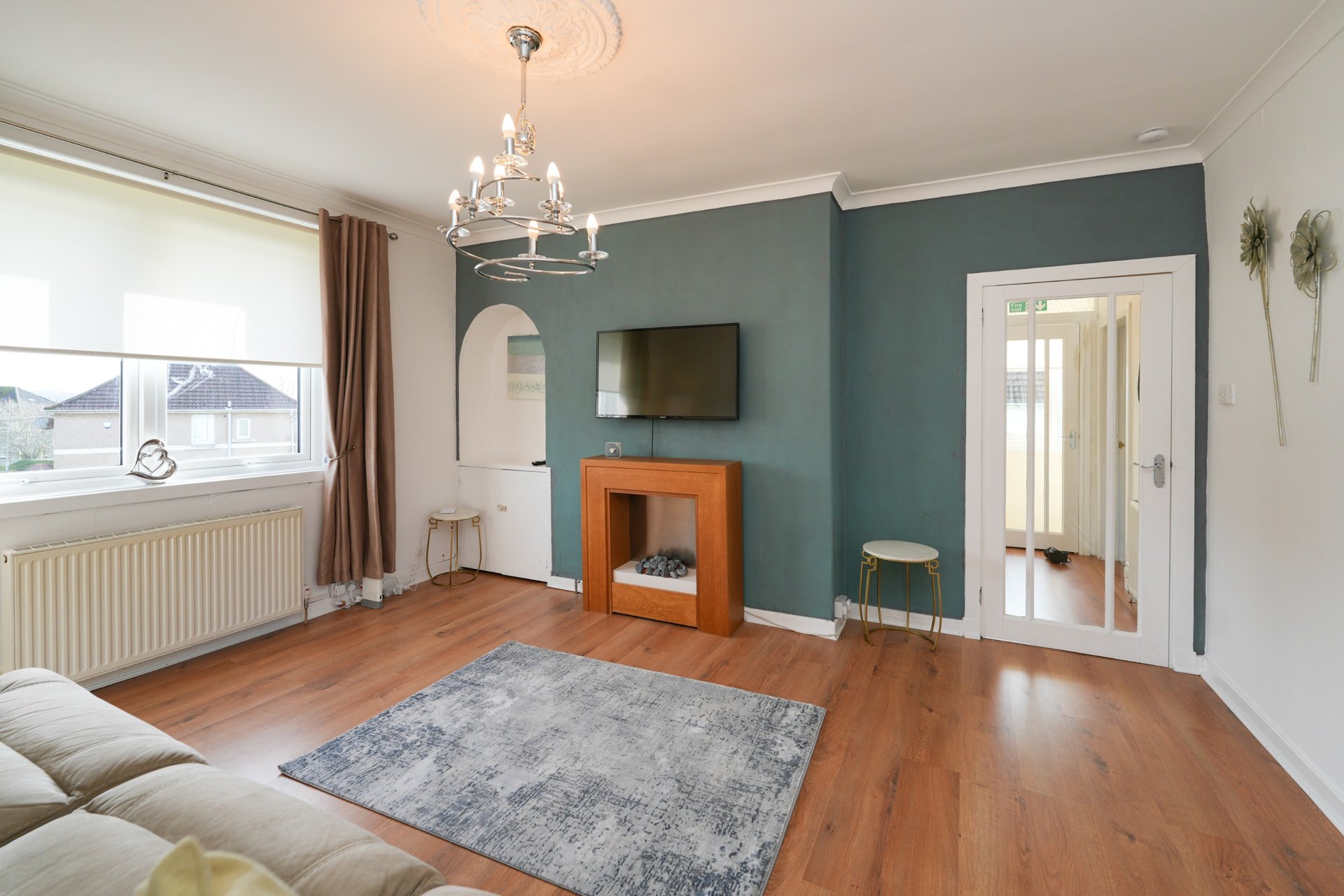 Spacious living room with wooden floor, teal accent wall, fireplace, chandelier and large windows