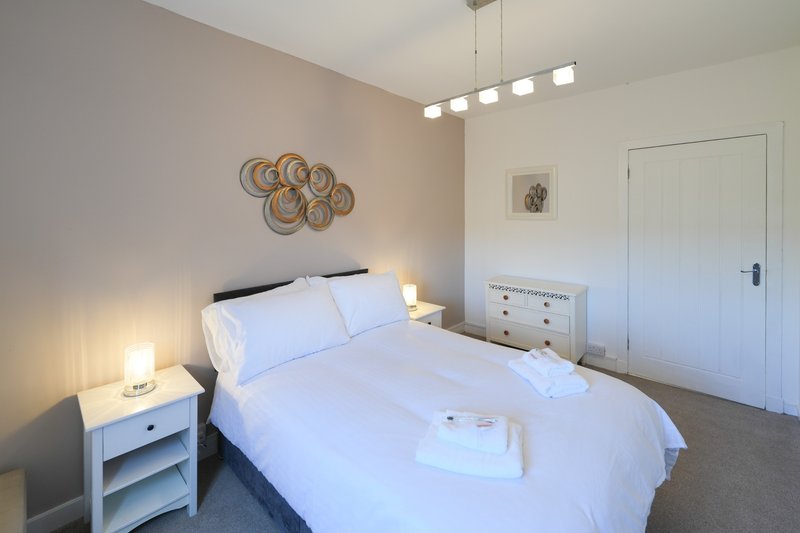 Bright bedroom with double bed, white bedding, woven wall art, and bedside lamps