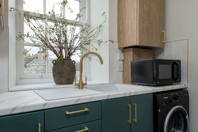 Modern kitchen with green cabinetry, marble countertop, potted plant arrangement and microwave