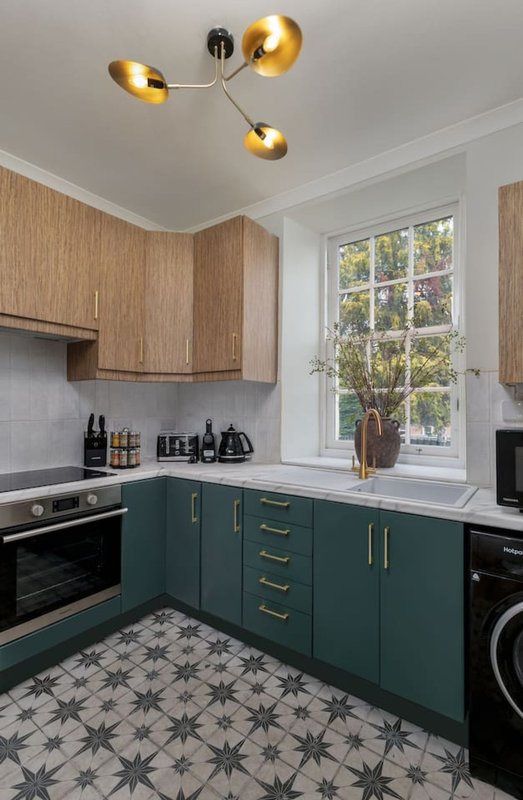 Modern kitchen with teal cabinetry, wood upper units, gold ceiling lights, patterned floor tiles