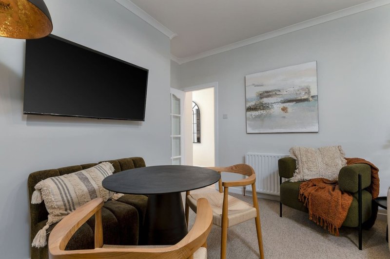 Modern living room with dining table, armchairs, wall-mounted TV and landscape artwork