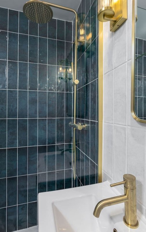 Modern bathroom with dark tiled shower enclosure, brass fixtures and white sink