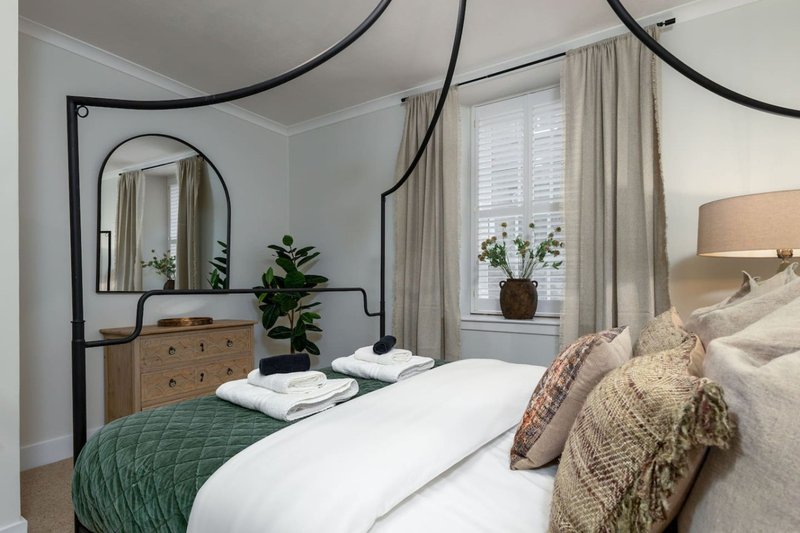 Bright bedroom with arched black metal bed frame, wooden dresser, and multiple decorative pillows and throws