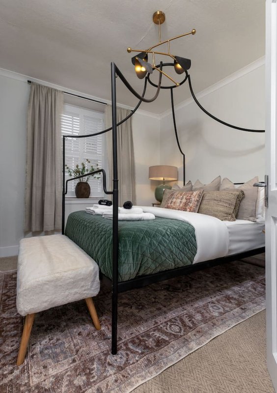 Bedroom with black four-poster bed, green quilted bedding, white pillows, modern ceiling light, and bedroom mirror