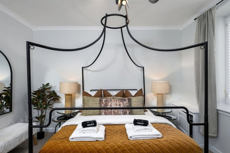 Modern bedroom with black four-poster canopy bed, gold bedding, and twin bedside lamps