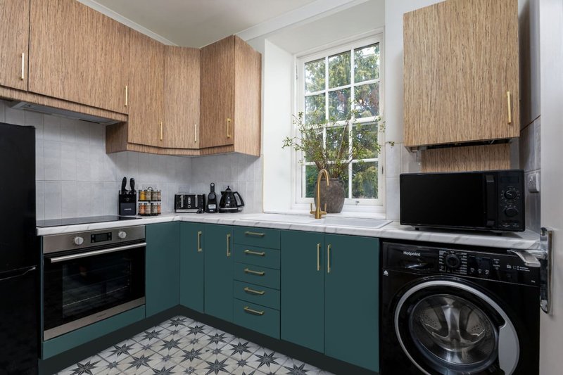 Modern kitchen with teal and wood cabinetry, black appliances, washing machine, and patterned floor tiles