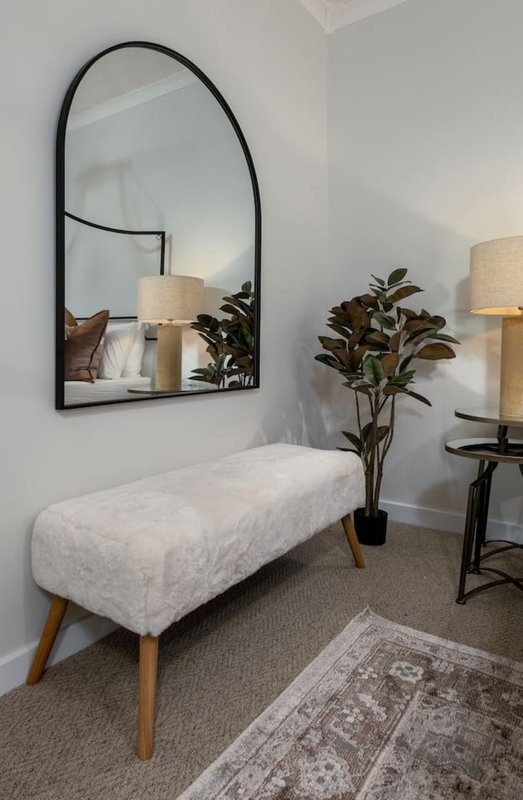 Modern bedroom corner with upholstered bench, arched mirror, potted plant and table lamps