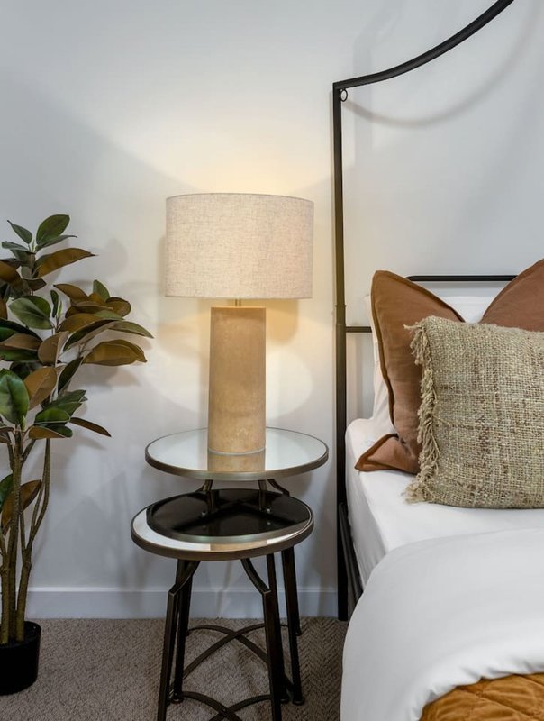 Bedroom corner with table lamp, potted plant, decorative pillows and white bedding