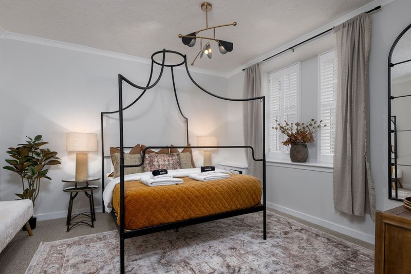 Modern bedroom with black canopy bed, mustard bedding, pendant lighting, and large windows with shutters