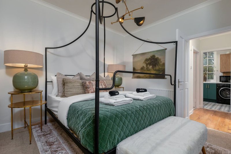 Bedroom with black four-poster bed, green bedding, bedside lamps, and ensuite bathroom visible