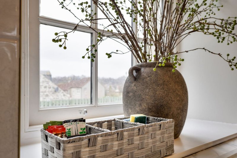 Windowsill with woven basket, large ceramic vase with dried branches, and view of hillside landscape