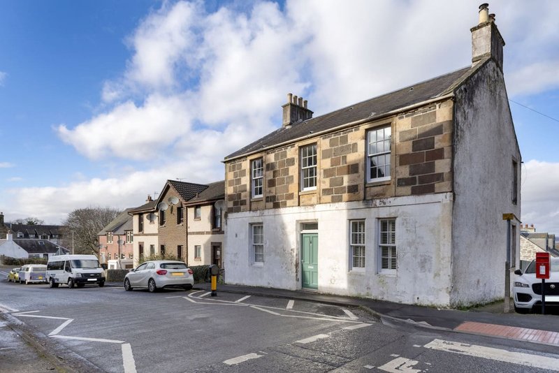 Stone and whitewashed buildings on a street corner with parked vehicles and clear sky
