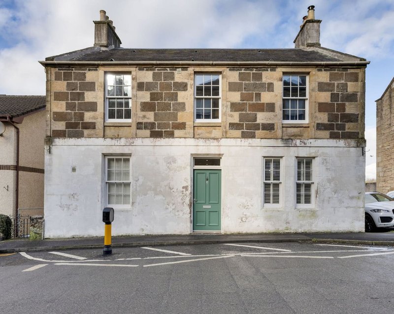Stone and rendered two-storey detached house with green door and driveway