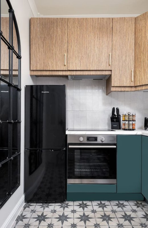 Modern kitchen with black refrigerator, wood cabinets, teal cabinetry, and patterned tile flooring