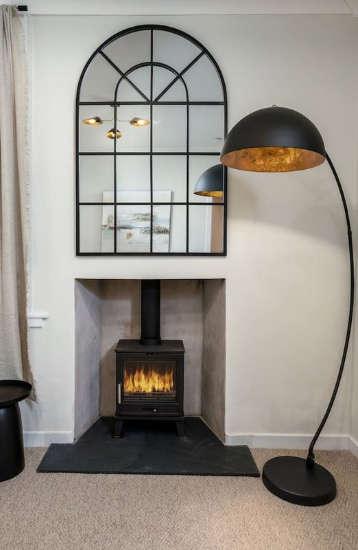 Living room with black wood-burning stove, arched window, floor lamp and fireplace hearth