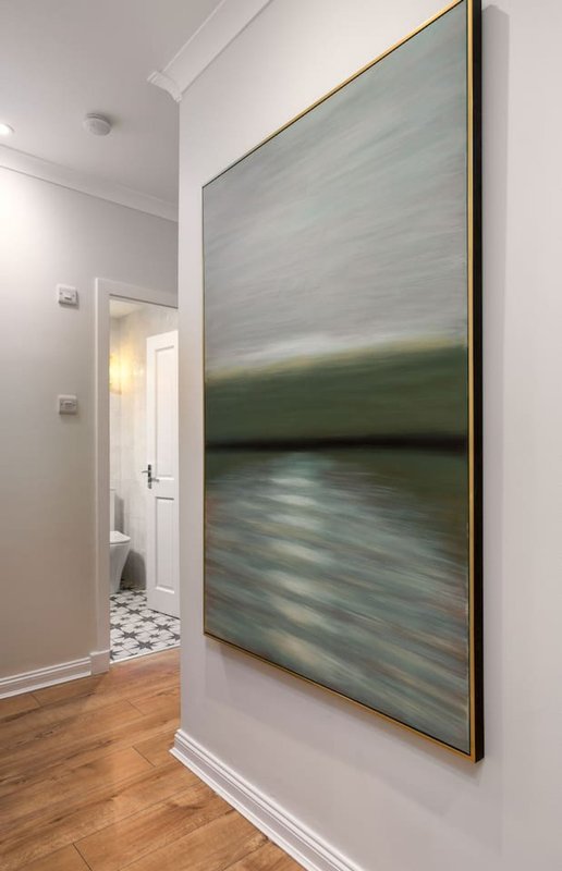 Modern hallway with framed abstract landscape artwork, white walls, wooden flooring and doorway